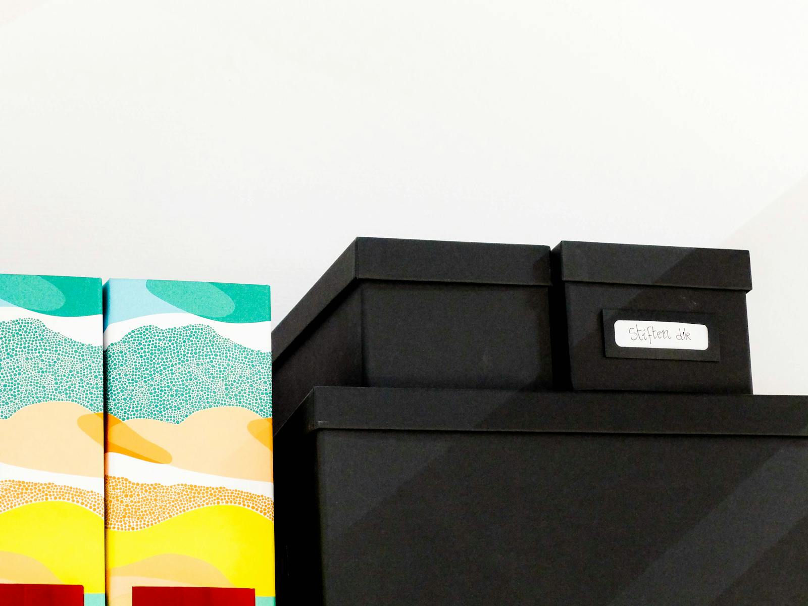 A stack of colorful and black storage boxes neatly arranged on a shelf.